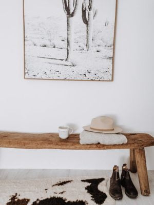 Wooden bench with hat placed in light corridor with carpet and picture in apartment in light minimalistic style
